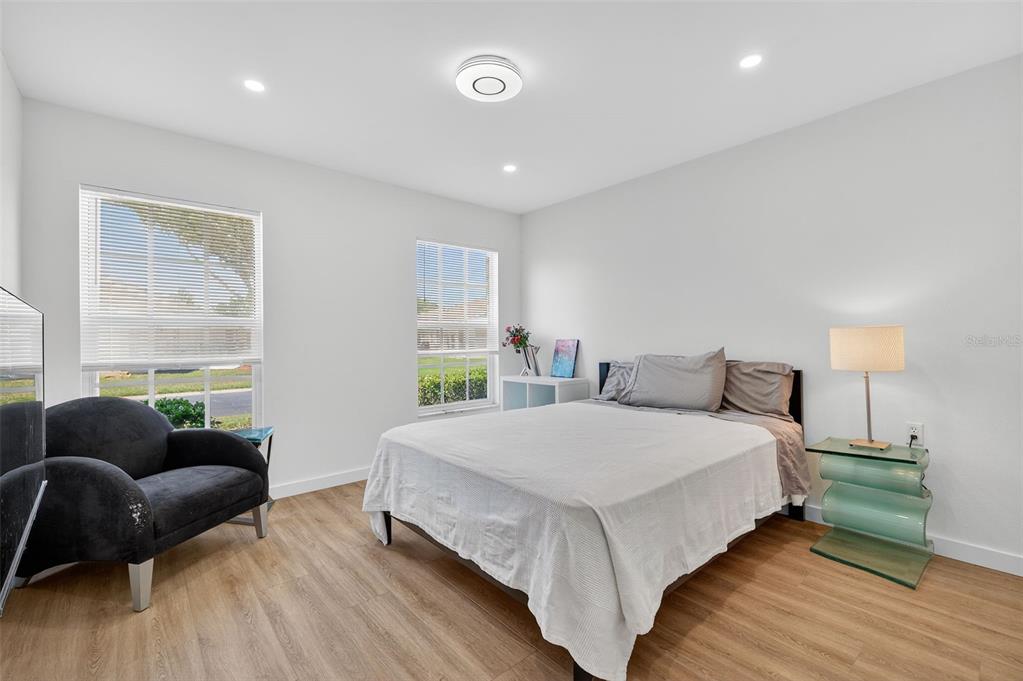 A bedroom features light wood-look flooring, white walls, two windows, and a bed with gray bedding — 4916 TROON LANE, NEW PORT RICHEY, FL