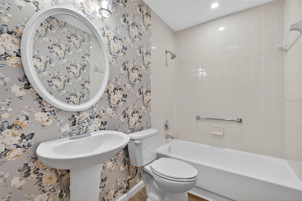 A bathroom features a pedestal sink, a toilet, and a tiled shower-tub combination with wallpaper — 4916 TROON LANE, NEW PORT RICHEY, FL