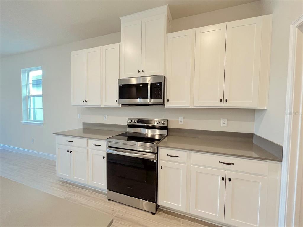A kitchen features white shaker cabinets, stainless steel appliances, and gray quartz countertops — 4961 RAIN SHADOW DRIVE, ST CLOUD, FL