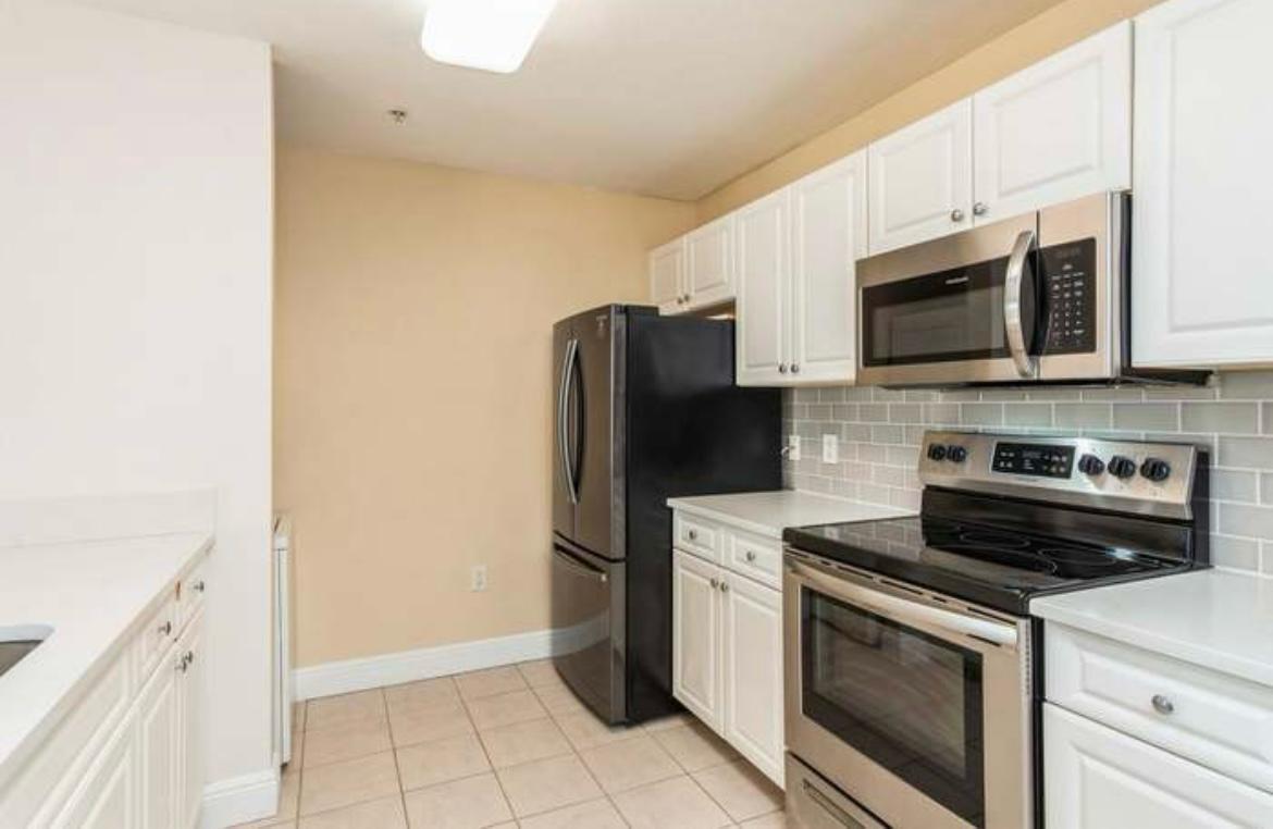 A kitchen with white cabinets, stainless steel appliances, a black refrigerator, and a tiled backsplash — 1200 Town Center Drive # 305, Jupiter FL 33458, JUPITER, FL
