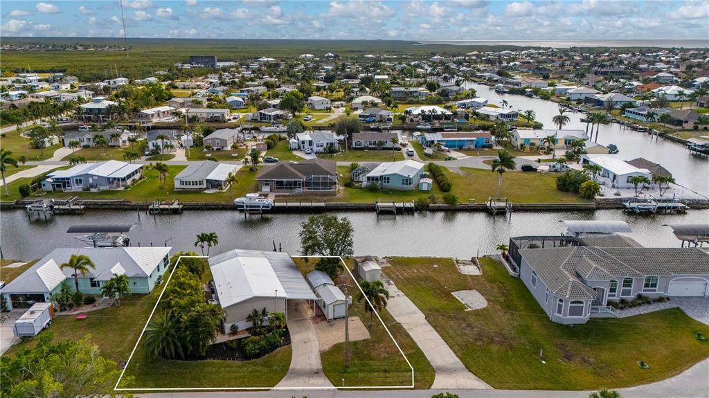 An aerial view shows a single-story house with a carport and shed along a canal — 751 LONGBEACH COURT, PUNTA GORDA, FL