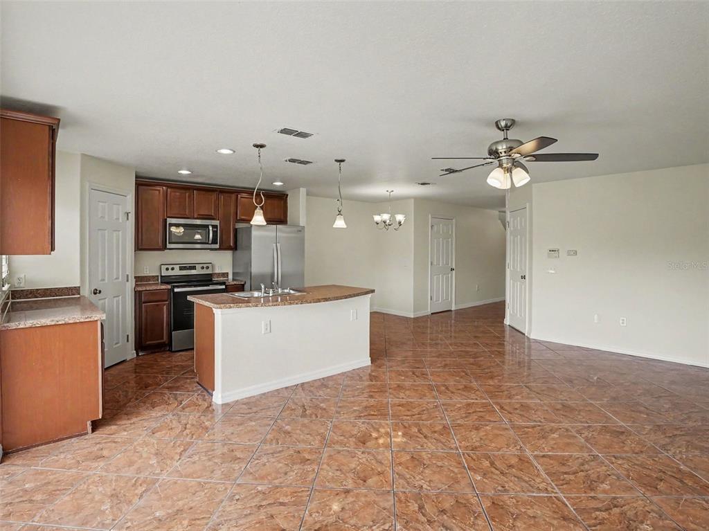 A kitchen with brown cabinets, stainless steel appliances, and a central island on tiled floors — 6105 TIMBER CREST DRIVE, ST CLOUD, FL