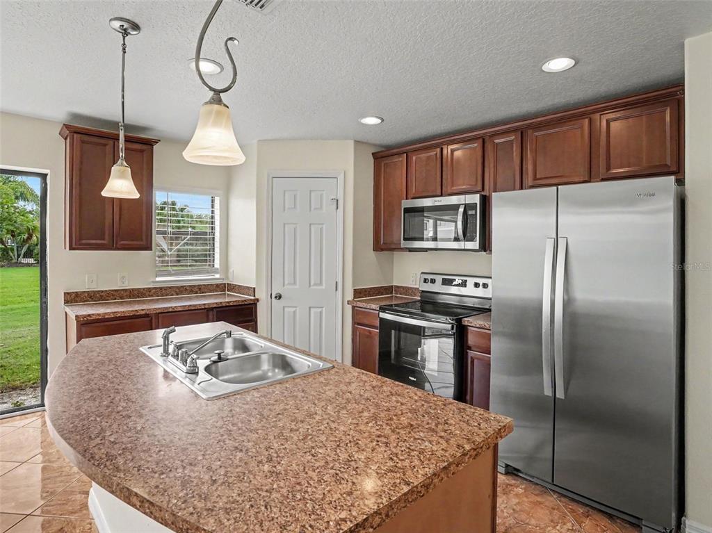 A kitchen with brown cabinets, stainless steel appliances, a granite island, and tile flooring — 6105 TIMBER CREST DRIVE, ST CLOUD, FL
