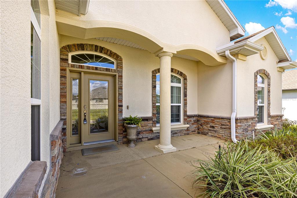 A covered front porch features a tan door with glass panels, stone accents, and columns — 17306 SE 112TH CT ROAD, SUMMERFIELD, FL