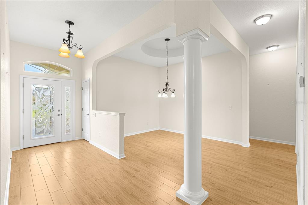 An entryway with light wood flooring leads to a dining area featuring a decorative column — 17306 SE 112TH CT ROAD, SUMMERFIELD, FL