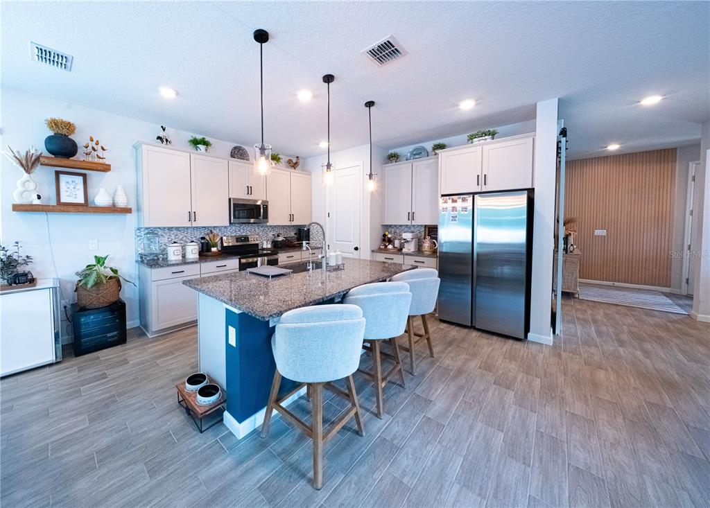 A kitchen features a blue island with bar seating, stainless steel appliances, and wood-look flooring — 4210 SOUTHERN VISTA LOOP, ST CLOUD, FL