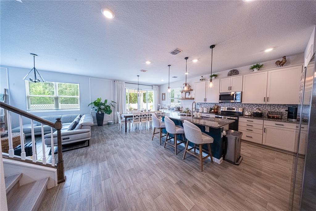 An open-concept kitchen and living area features a large island, light cabinetry, and wood-look flooring — 4210 SOUTHERN VISTA LOOP, ST CLOUD, FL