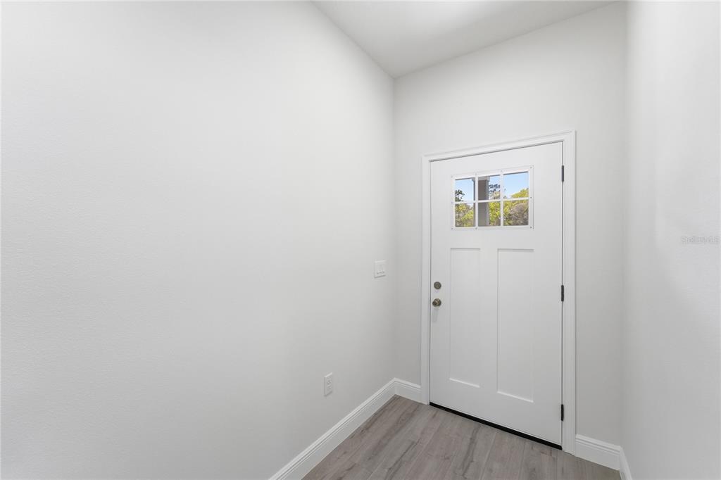 An empty entryway features white walls, gray wood-look flooring, and a white exterior door — 15811 SW 59TH AVENUE ROAD, OCALA, FL