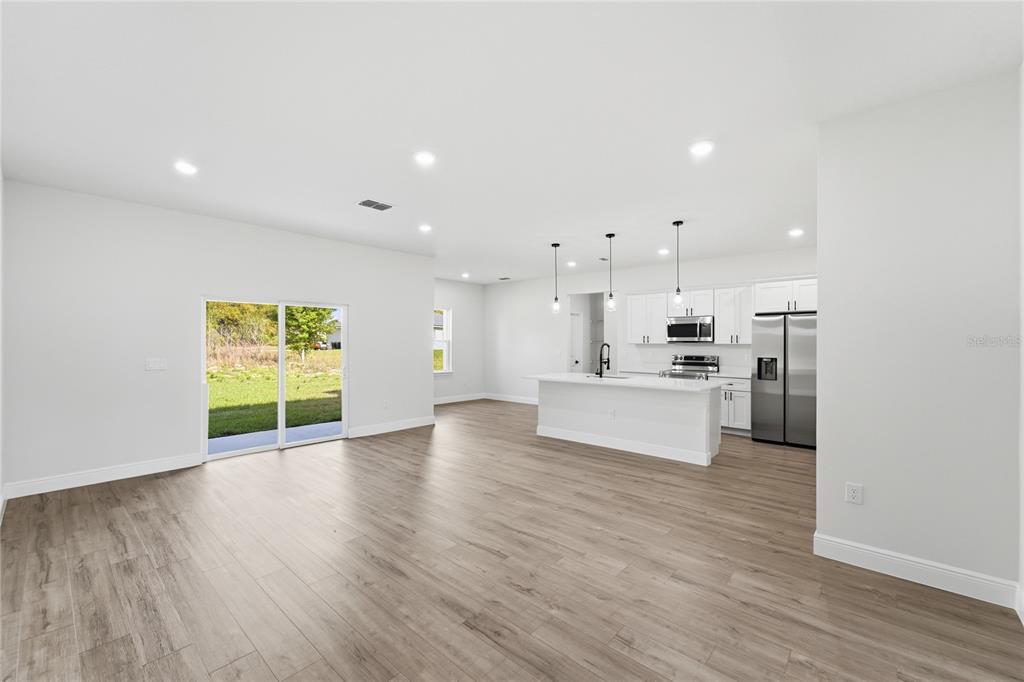 An open-concept kitchen and living area features white cabinetry, stainless steel appliances, and wood-look flooring — 15811 SW 59TH AVENUE ROAD, OCALA, FL