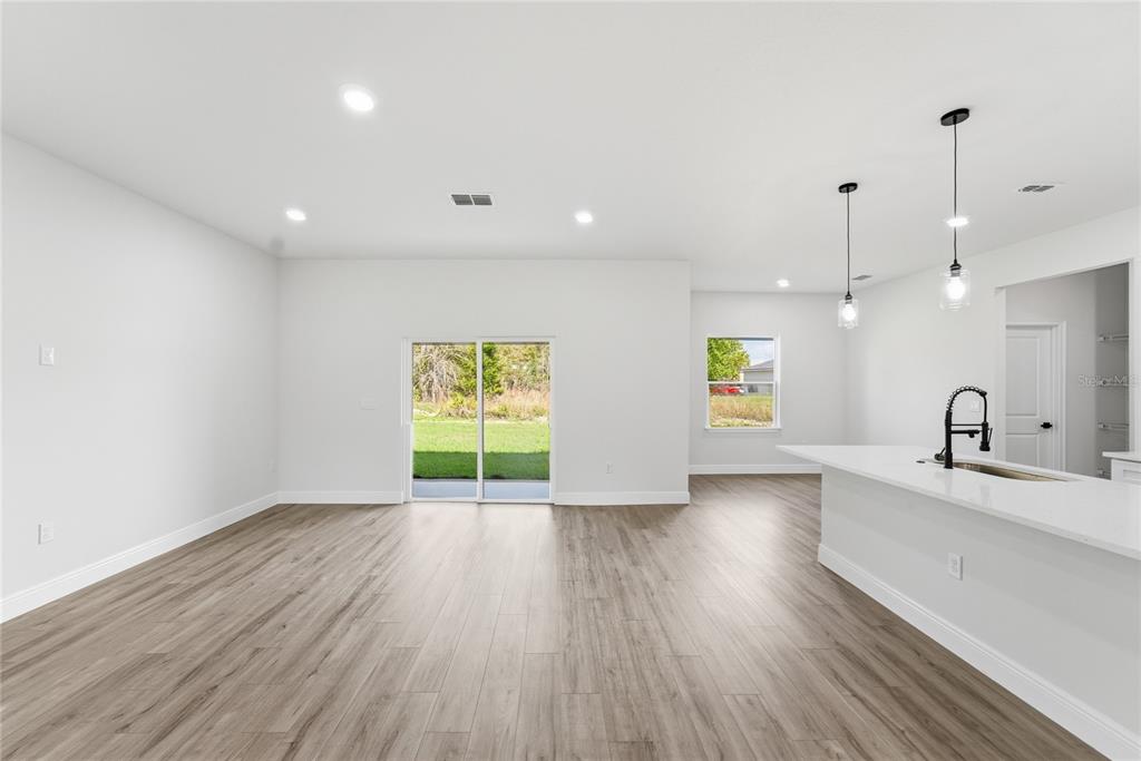 A bright, open-concept living area features light wood-look flooring, white walls, and a sliding glass door — 15811 SW 59TH AVENUE ROAD, OCALA, FL