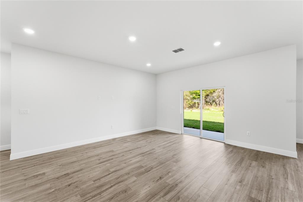 An empty room features light wood-look flooring, white walls, recessed lighting, and a sliding glass door — 15811 SW 59TH AVENUE ROAD, OCALA, FL