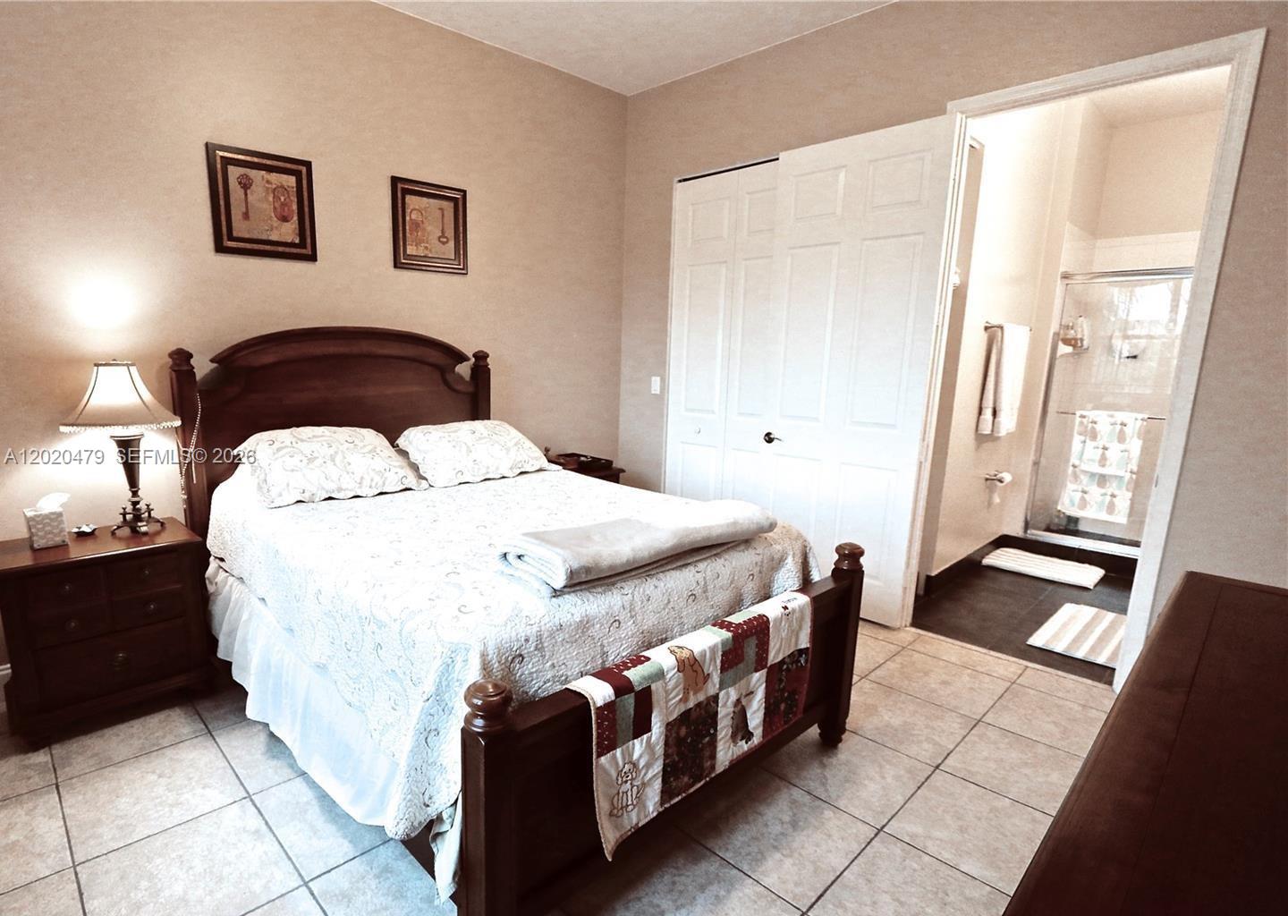 A bedroom with a wooden bed frame, tiled floors, and an attached bathroom — 4602 SW 160th Ave # 533, Miramar FL 33027, MIRAMAR, FL