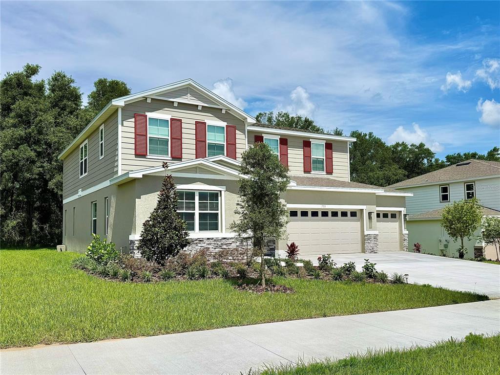 A two-story suburban house with beige siding, red shutters, and a three-car garage — 733 WEKIVA RIDGE DRIVE, MOUNT DORA, FL