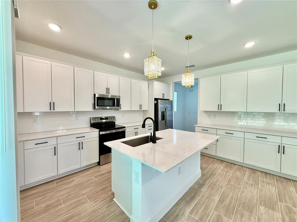 A modern kitchen features white cabinetry, quartz countertops, a center island, and wood-look tile flooring — 733 WEKIVA RIDGE DRIVE, MOUNT DORA, FL