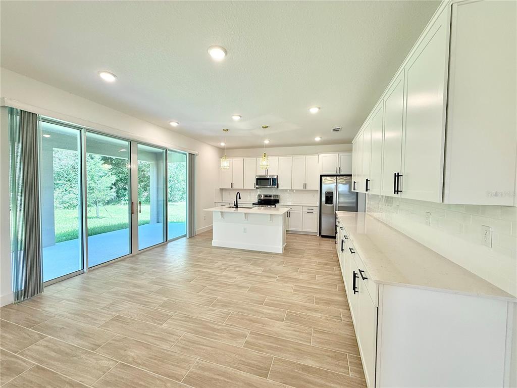 A modern kitchen features white cabinetry, a central island, and sliding glass doors to a patio — 733 WEKIVA RIDGE DRIVE, MOUNT DORA, FL