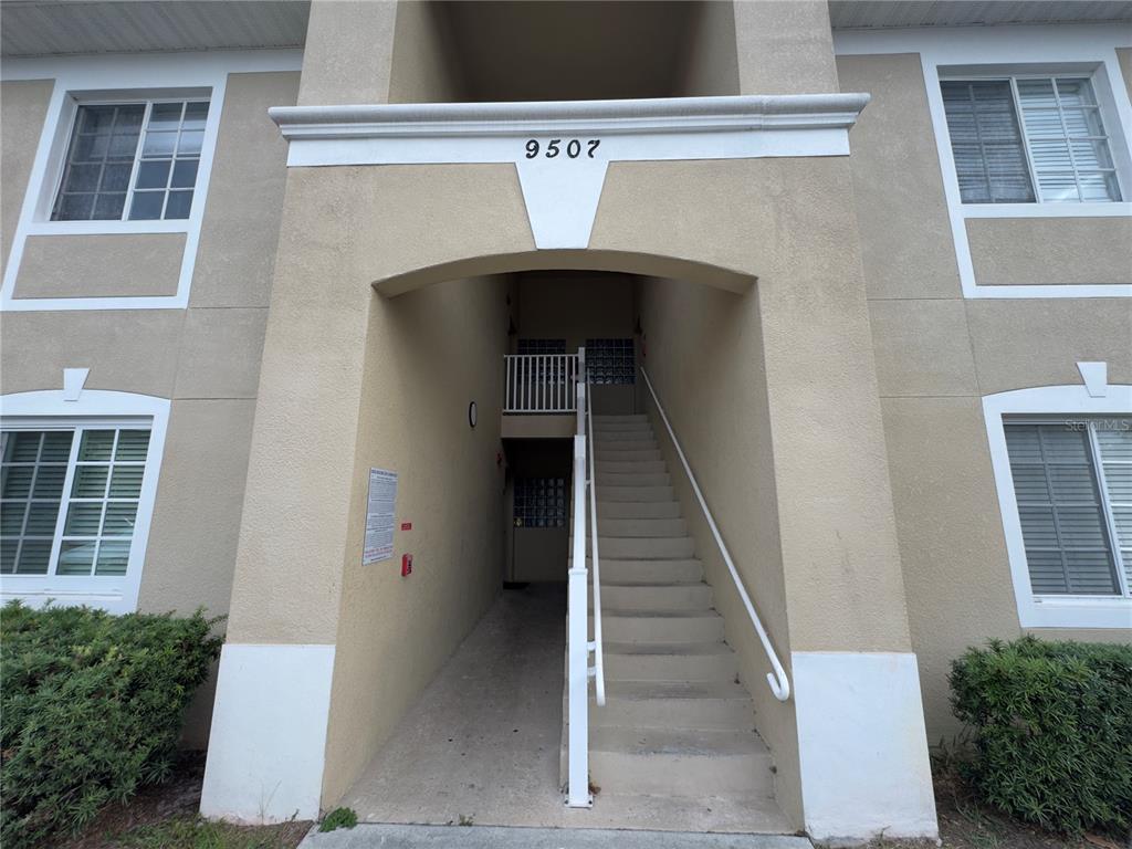 The exterior of a multi-story apartment building features a central staircase leading to upper units — 9507 AMBERDALE COURT UNIT 201, RIVERVIEW, FL