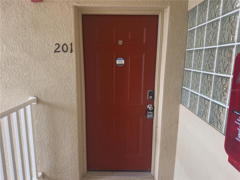 A red front door with a digital lock and a Ring sticker labeled 201 — 9507 AMBERDALE COURT UNIT 201, RIVERVIEW, FL