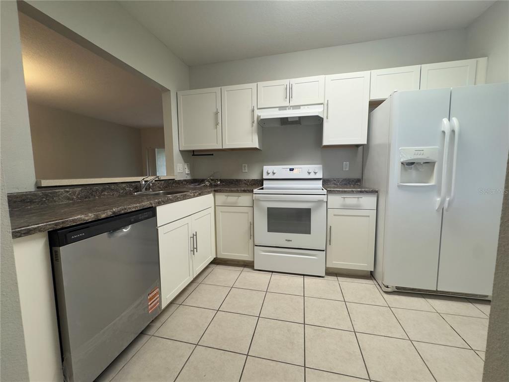 A kitchen features white cabinets, a stainless steel dishwasher, a white stove, and tile flooring — 9507 AMBERDALE COURT UNIT 201, RIVERVIEW, FL