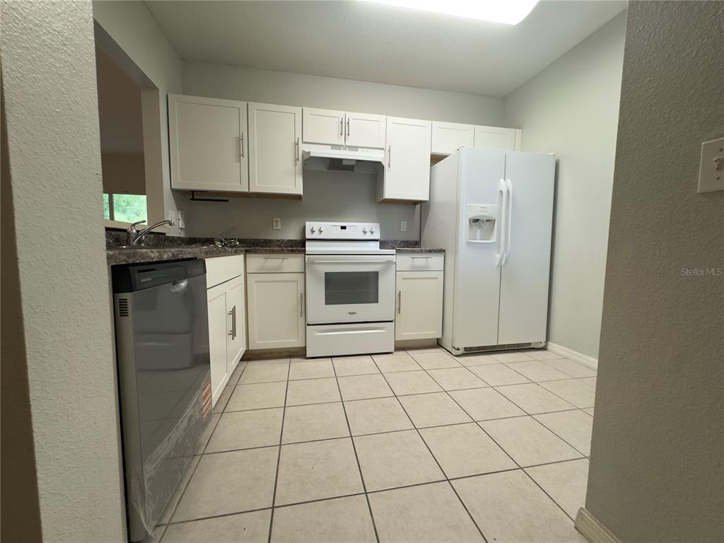 A kitchen features white cabinets, white appliances, dark countertops, and light-colored tile flooring — 9507 AMBERDALE COURT UNIT 201, RIVERVIEW, FL
