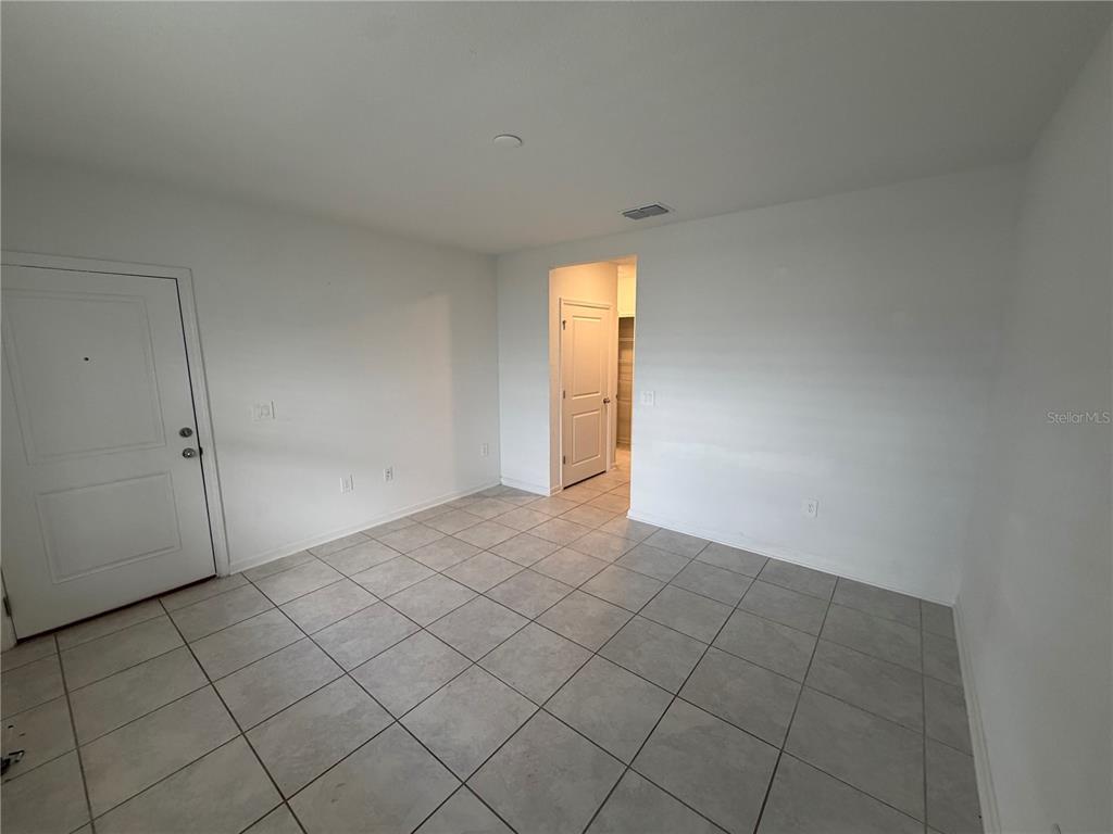 An empty room features white walls, light-colored tile flooring, a white entry door, and a doorway — 314 LAWSON AVENUE UNIT Rear, HAINES CITY, FL
