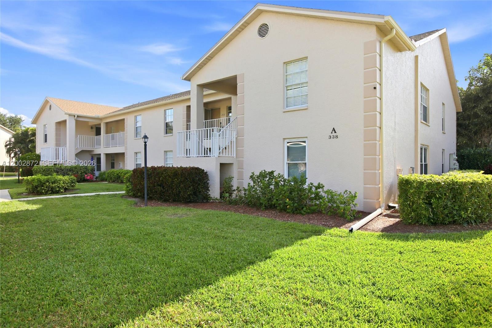 A two-story apartment building features beige stucco walls, white railings, and a landscaped lawn — 338 Bradstrom Cir # 104, Naples FL 34113, NAPLES, FL