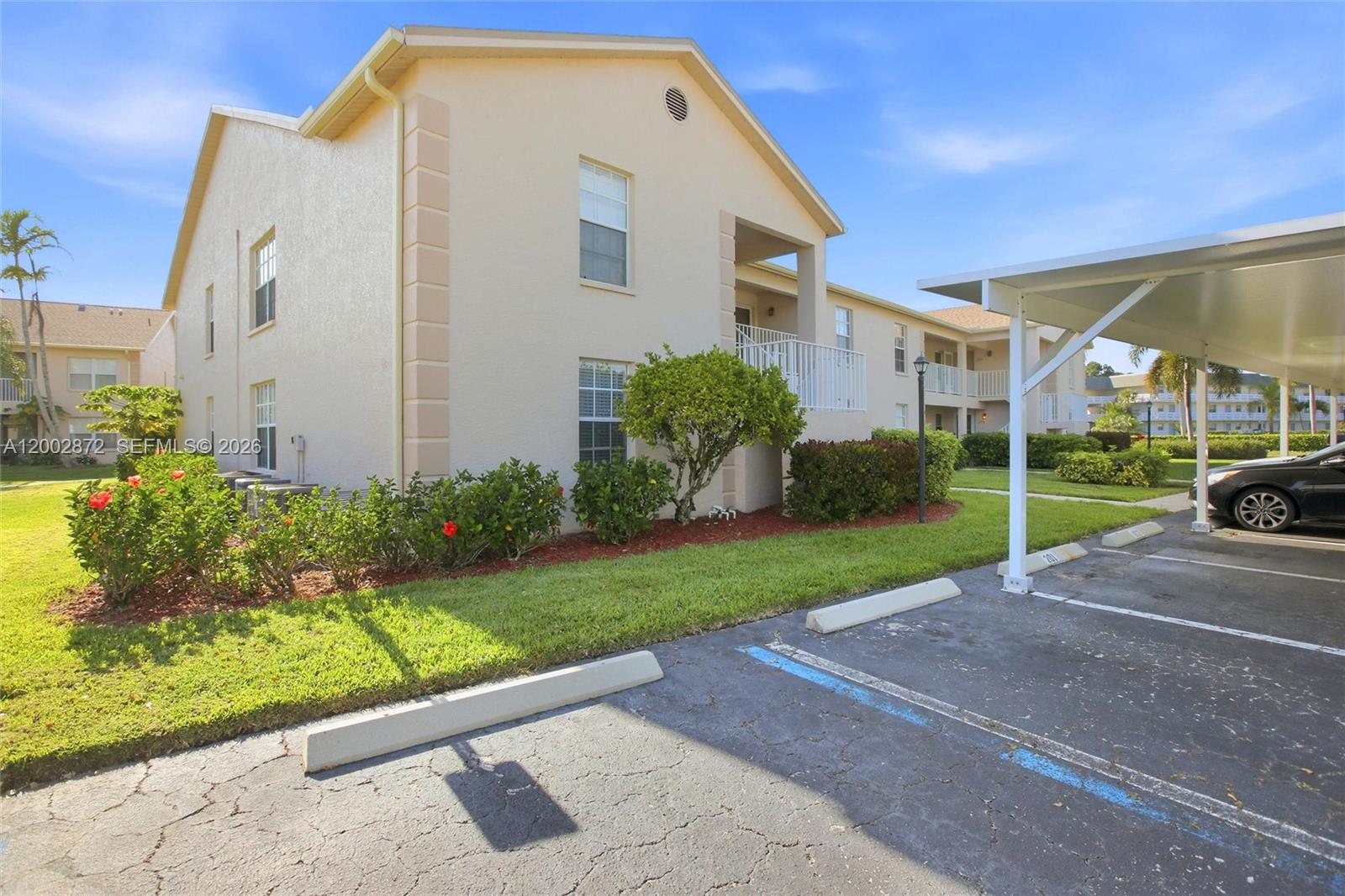 A two-story beige apartment building features a covered parking area and landscaped front yard — 338 Bradstrom Cir # 104, Naples FL 34113, NAPLES, FL