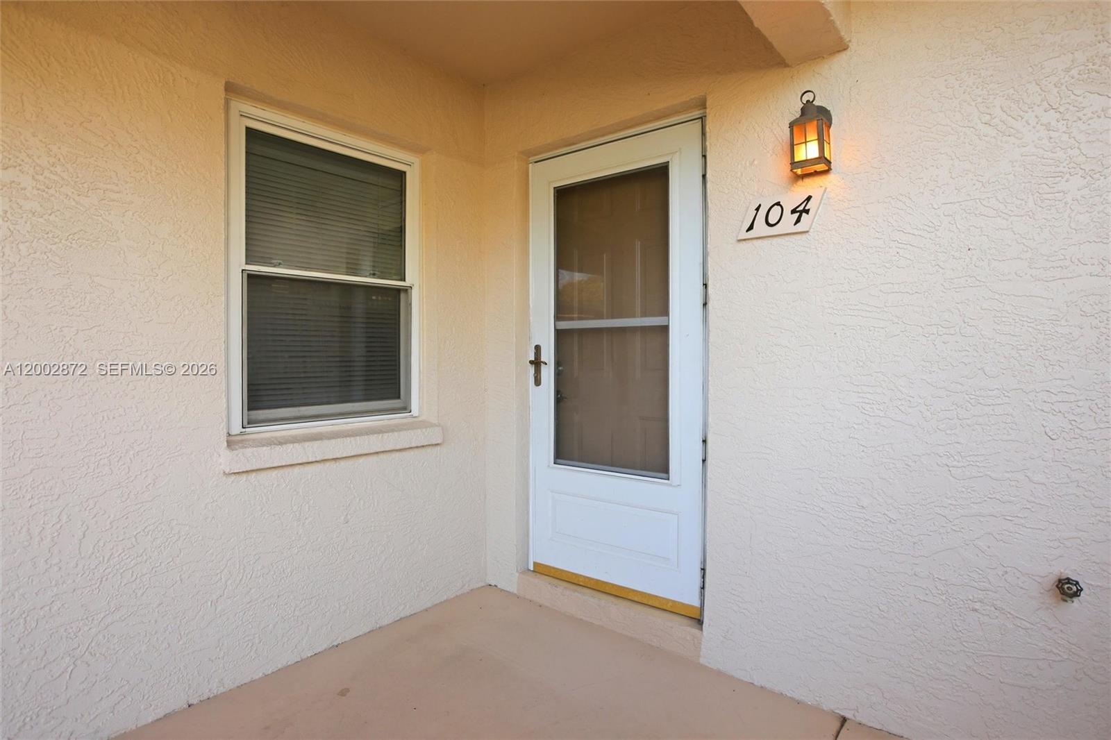 A beige exterior wall features a white storm door, a window, and house number 104 — 338 Bradstrom Cir # 104, Naples FL 34113, NAPLES, FL