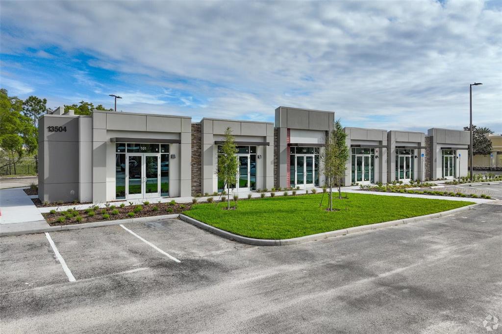 A modern, single-story commercial building with multiple glass-fronted entrances and a paved parking lot — 13504 VILLAGE PARK DRIVE UNIT 103, ORLANDO, FL