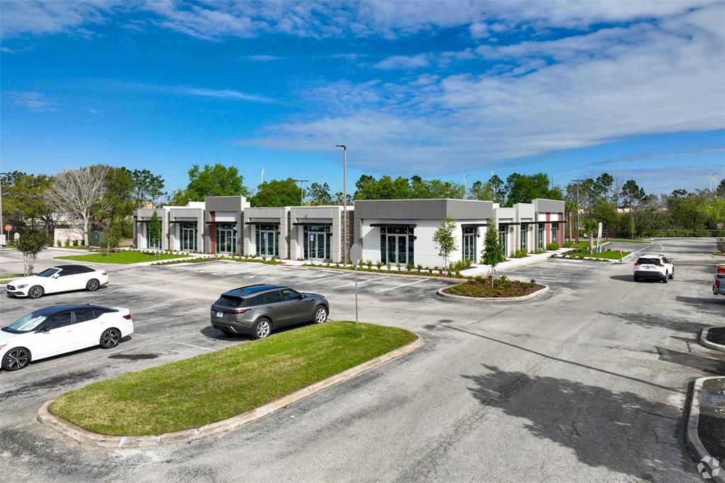A modern, single-story commercial building with glass storefronts sits in a paved parking lot — 13504 VILLAGE PARK DRIVE UNIT 103, ORLANDO, FL