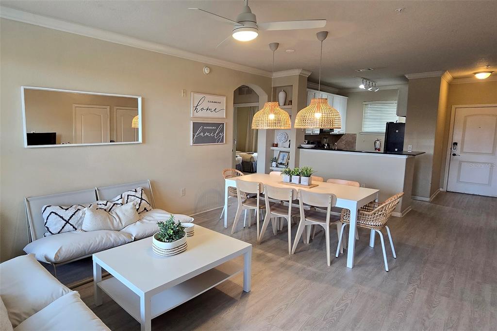 An open-concept living and dining area features light wood flooring, wicker pendant lights, and furniture — 912 CHARO PARKWAY UNIT 233, DAVENPORT, FL
