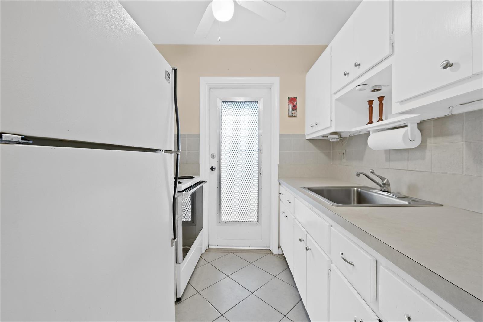 A galley kitchen features white cabinets, a stainless steel sink, and a white exterior door — 2750 W Golf Boulevard # 233, Pompano Beach FL 33064, POMPANO BEACH, FL