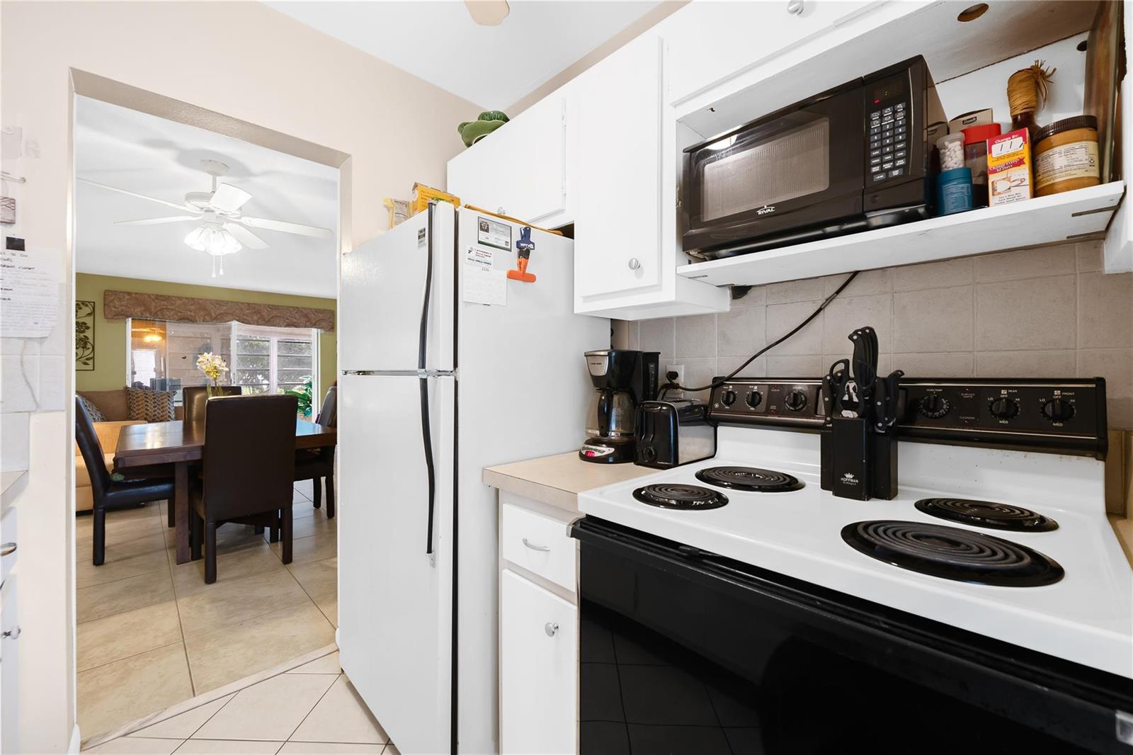A kitchen with white appliances and cabinets, a black stove, and a view into a dining room — 2750 W Golf Boulevard # 233, Pompano Beach FL 33064, POMPANO BEACH, FL