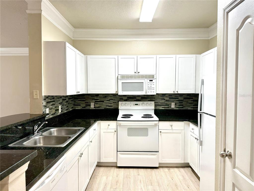 A kitchen features white cabinets, black countertops, a tiled backsplash, and white appliances — 8842 VILLA VIEW CIRCLE UNIT 3, ORLANDO, FL