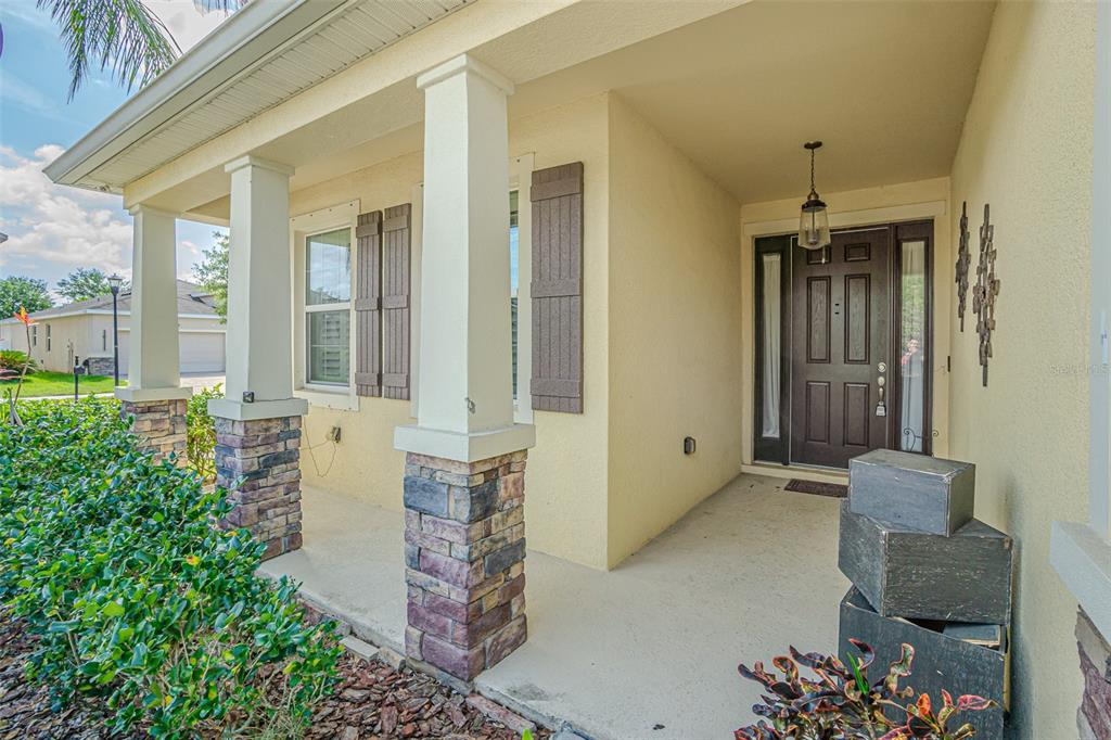 A covered front porch features stone-based columns, a dark wood front door, and beige siding — 10627 SCENIC HOLLOW DRIVE, RIVERVIEW, FL