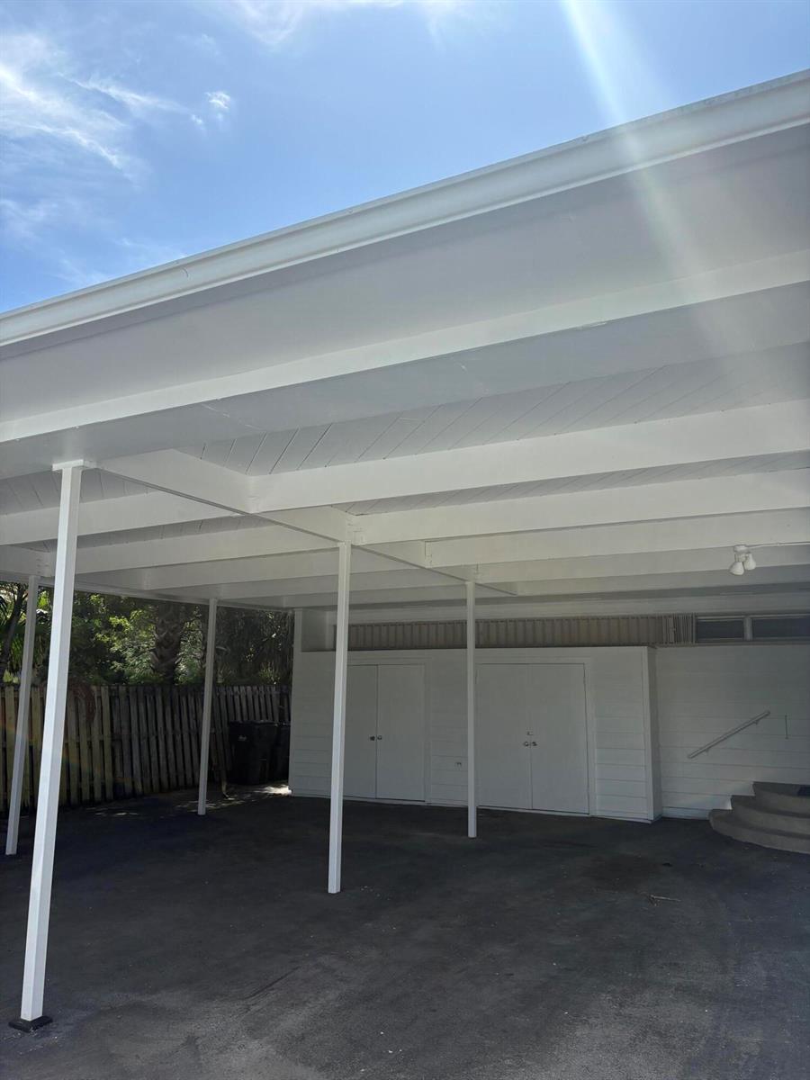 A covered carport features white support beams and walls with two sets of double doors — 202 Palm Court, Delray Beach FL 33444, DELRAY BEACH, FL