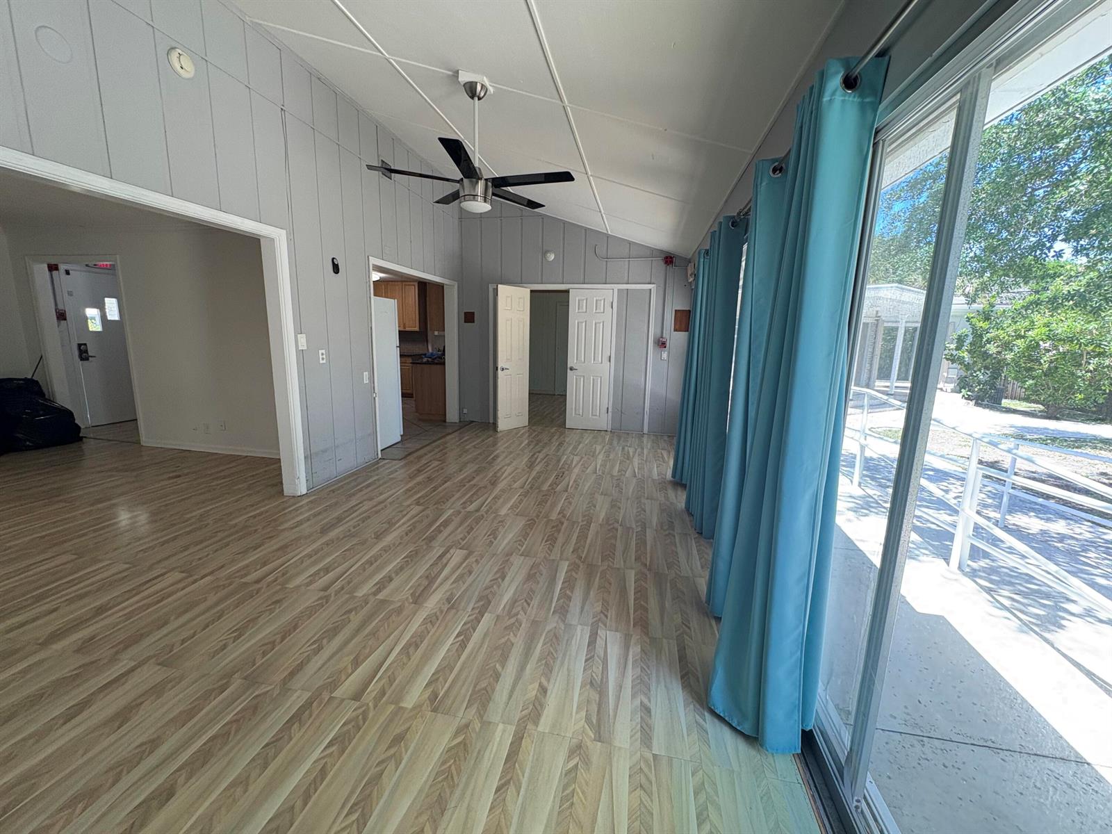 A living room with wood-look flooring, a ceiling fan, and sliding glass doors with curtains — 202 Palm Court, Delray Beach FL 33444, DELRAY BEACH, FL