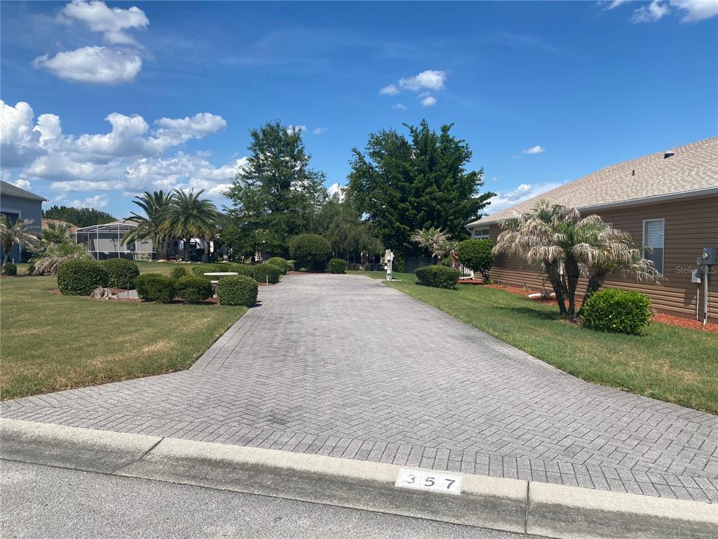 A paved driveway leads toward a house with landscaping and palm trees under a blue sky — 357 TRAVELERS DRIVE, POLK CITY, FL