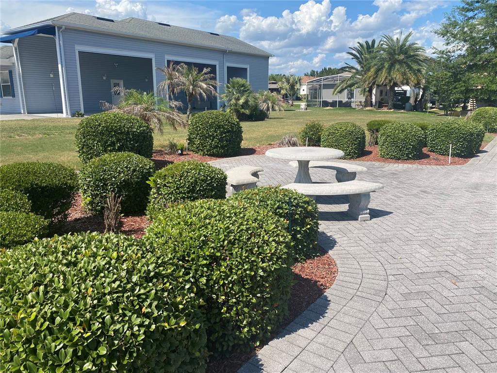 A paved patio features a stone table and benches surrounded by manicured shrubs and lawn — 357 TRAVELERS DRIVE, POLK CITY, FL