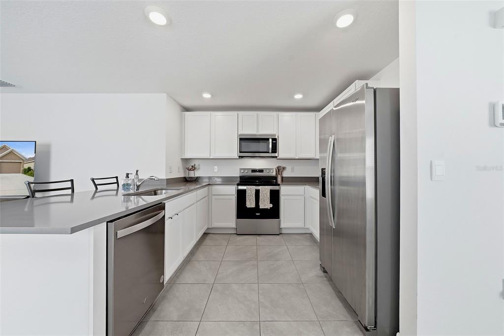 A modern kitchen features white cabinets, stainless steel appliances, gray countertops, and light tile flooring — 37396 SHARKS EYE LANE, ZEPHYRHILLS, FL