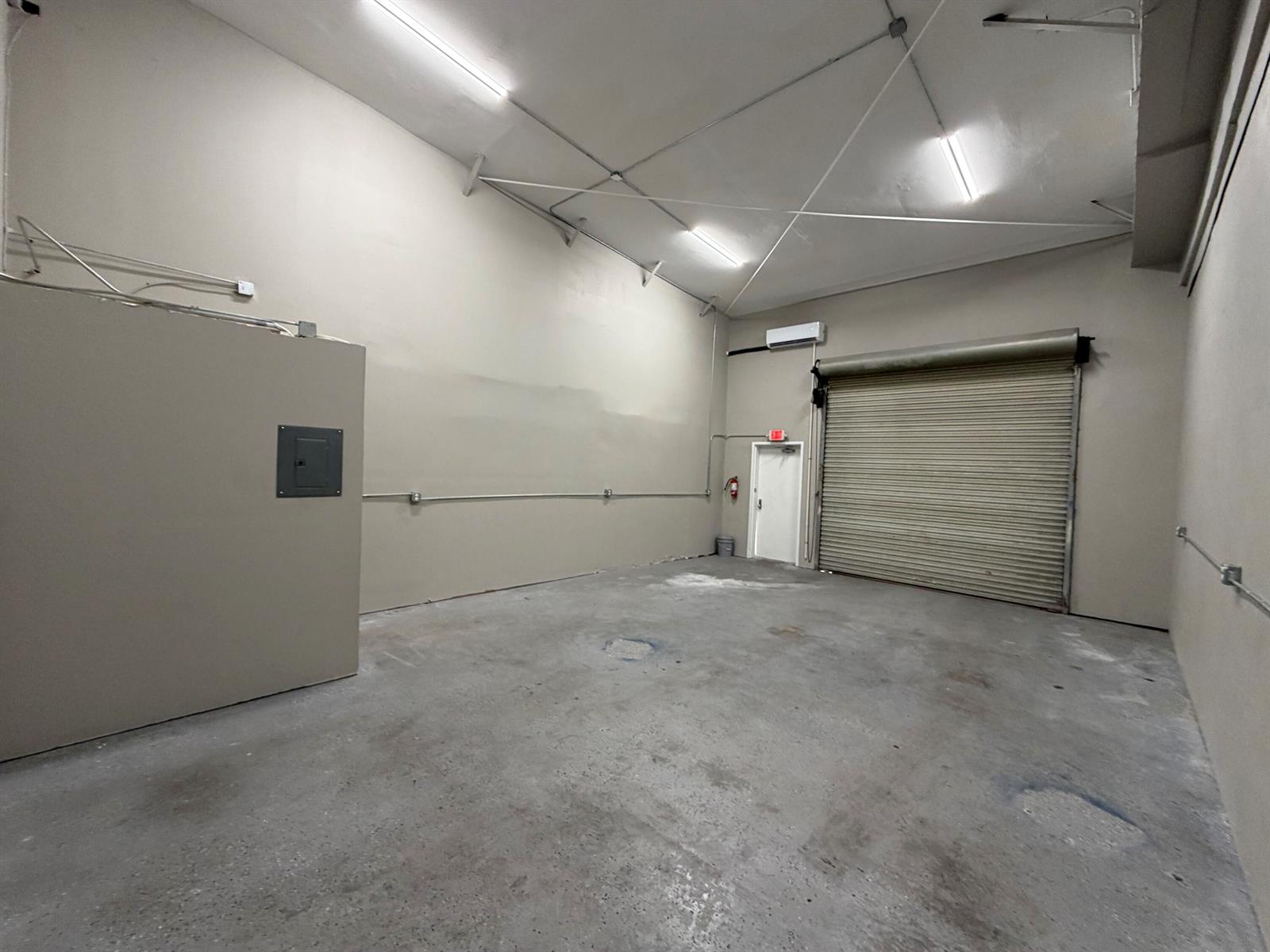 An empty industrial warehouse space features concrete floors, a roll-up door, and a side entrance — 1173b SW 1st Way, Deerfield Beach FL 33441, DEERFIELD BEACH, FL