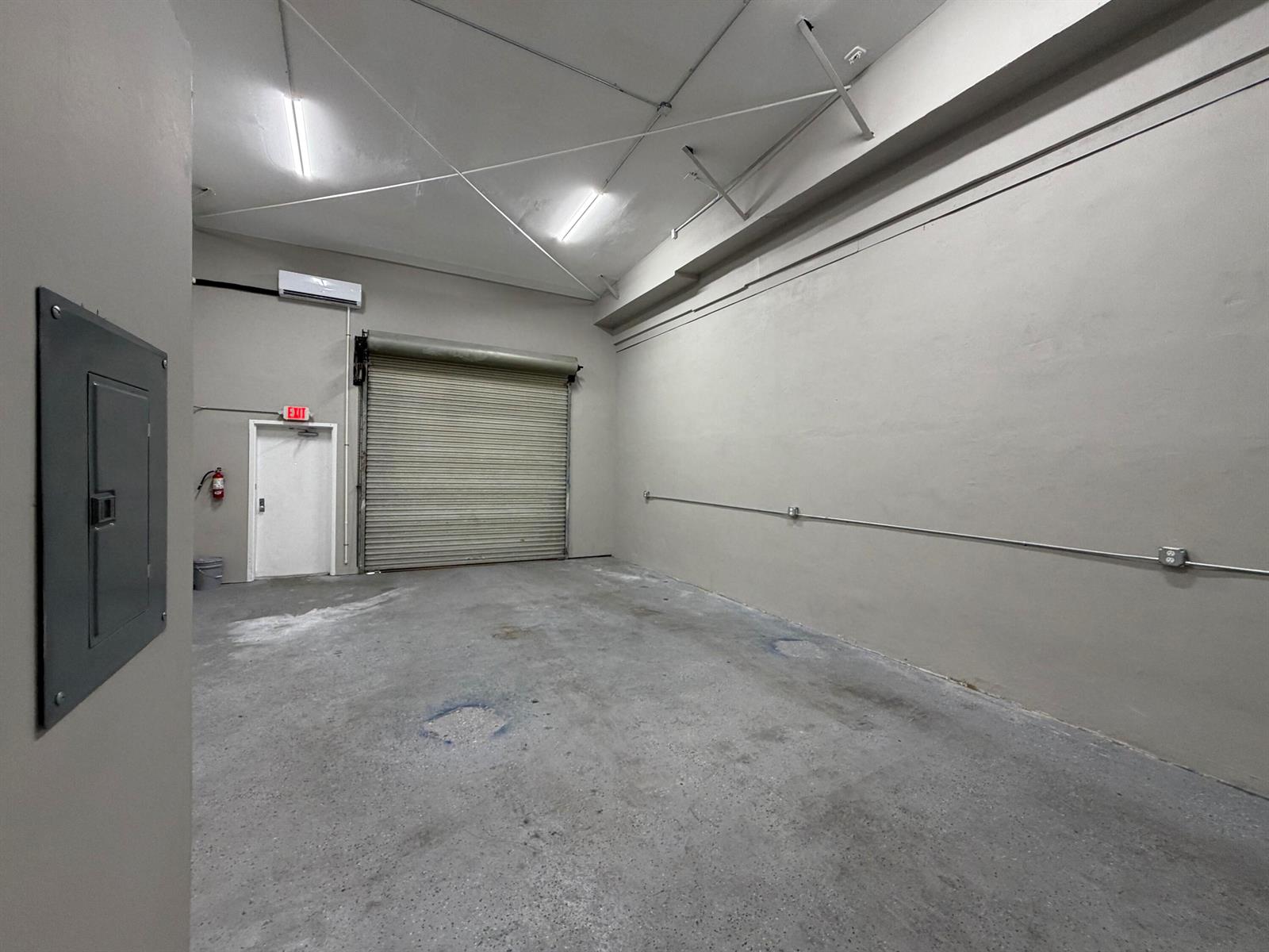 An empty industrial space features a concrete floor, a roll-up door, and an exit door — 1173b SW 1st Way, Deerfield Beach FL 33441, DEERFIELD BEACH, FL