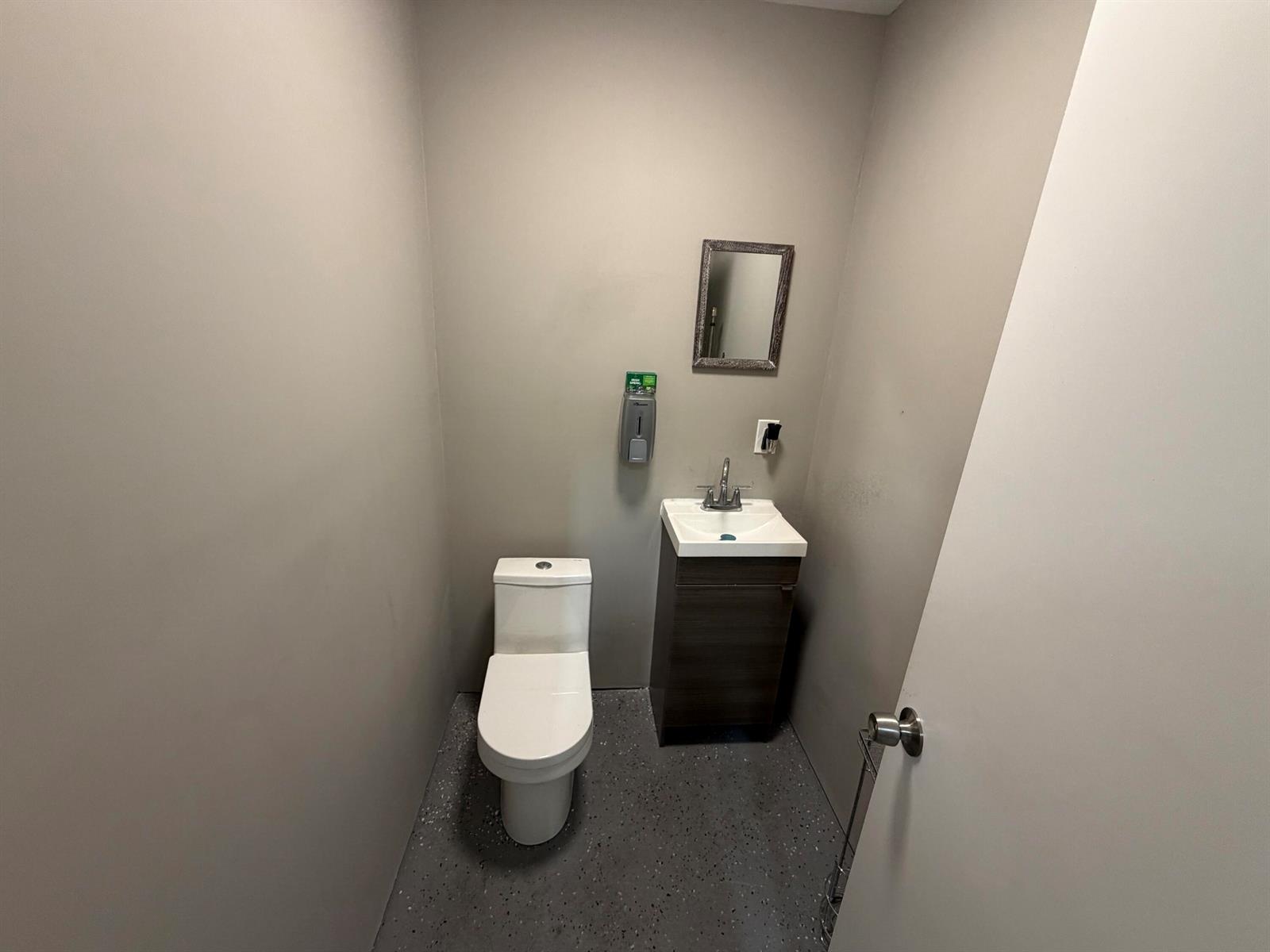 A small bathroom features a white toilet, a dark wood vanity, and gray flooring — 1173b SW 1st Way, Deerfield Beach FL 33441, DEERFIELD BEACH, FL
