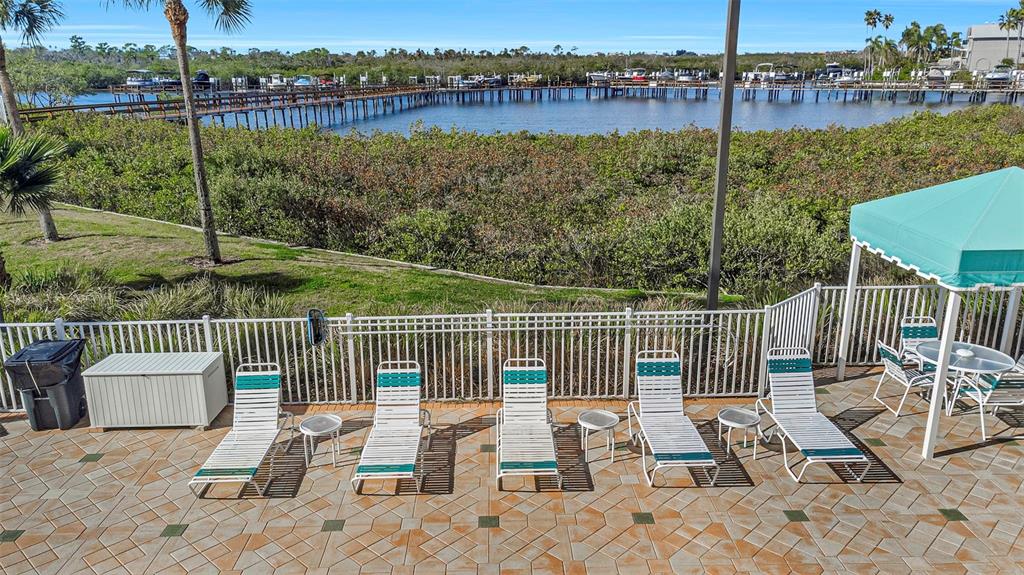 A patio with lounge chairs overlooks a fenced-in area, mangroves, and a boat dock — 4516 SEAGULL DRIVE UNIT 313, NEW PORT RICHEY, FL