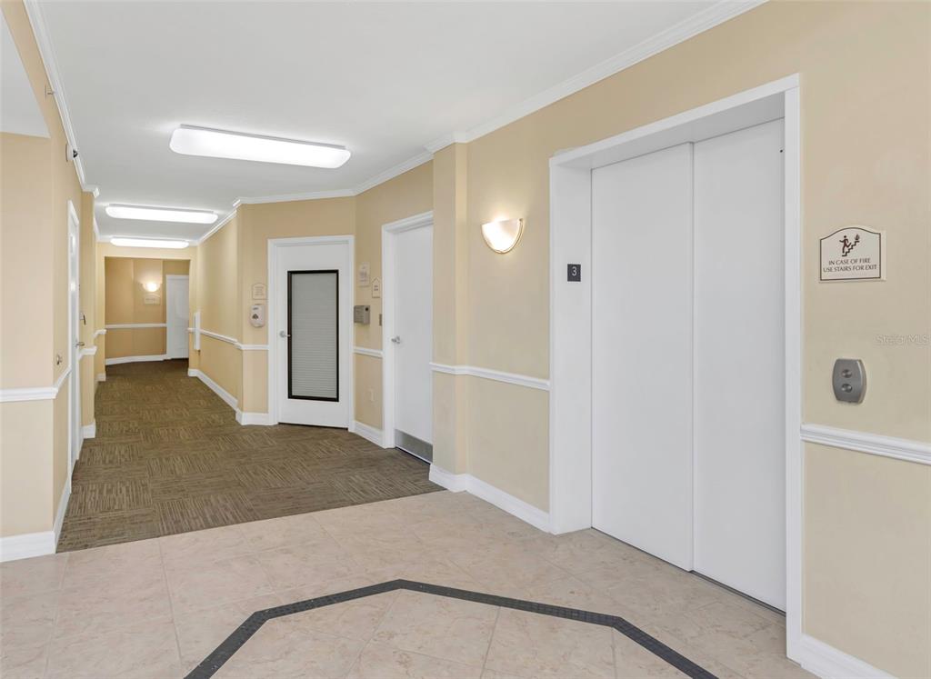 An indoor hallway features beige walls, tile flooring, an elevator, and several closed doors — 4516 SEAGULL DRIVE UNIT 313, NEW PORT RICHEY, FL