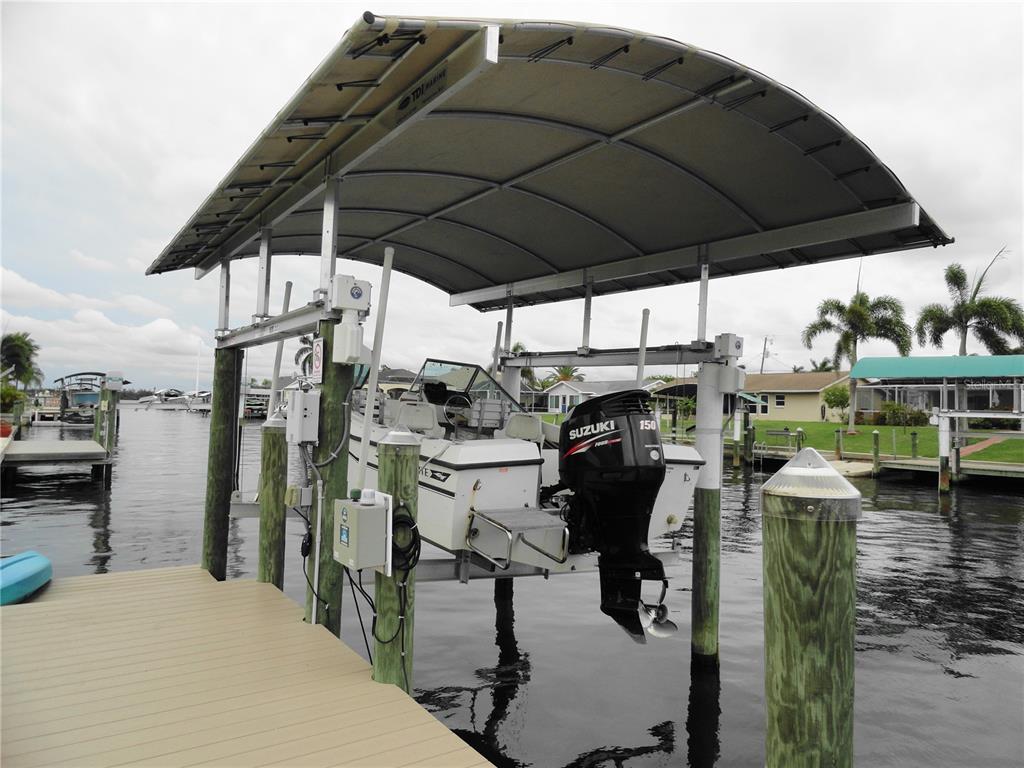 A boat is lifted on a mechanical dock system under a canopy cover over water — 5226 NEVILLE TERRACE, PORT CHARLOTTE, FL