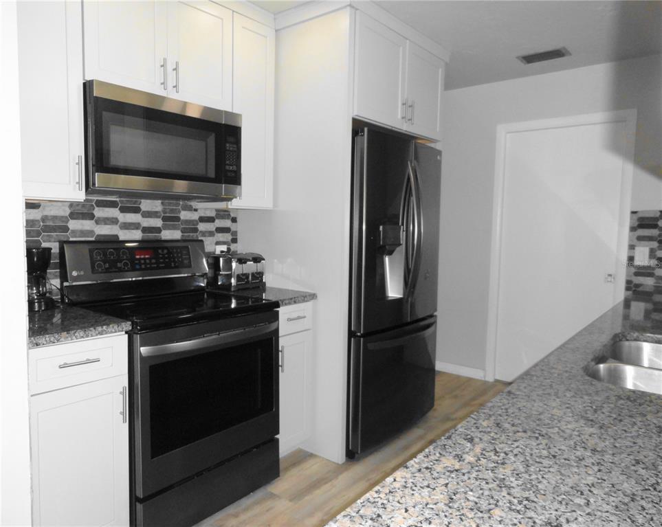 A kitchen features white cabinets, black appliances, granite countertops, and a gray tiled backsplash — 5226 NEVILLE TERRACE, PORT CHARLOTTE, FL