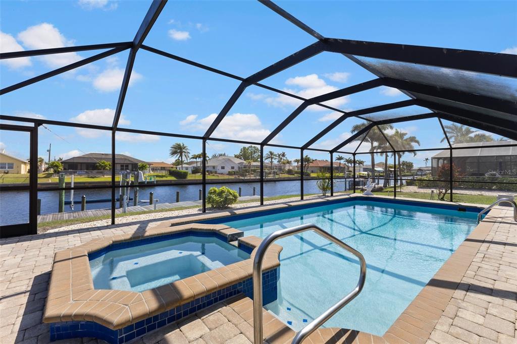 A screened-in pool and hot tub overlooking a canal with a dock and neighboring houses — 4196 EASTLAKE COURT, PORT CHARLOTTE, FL