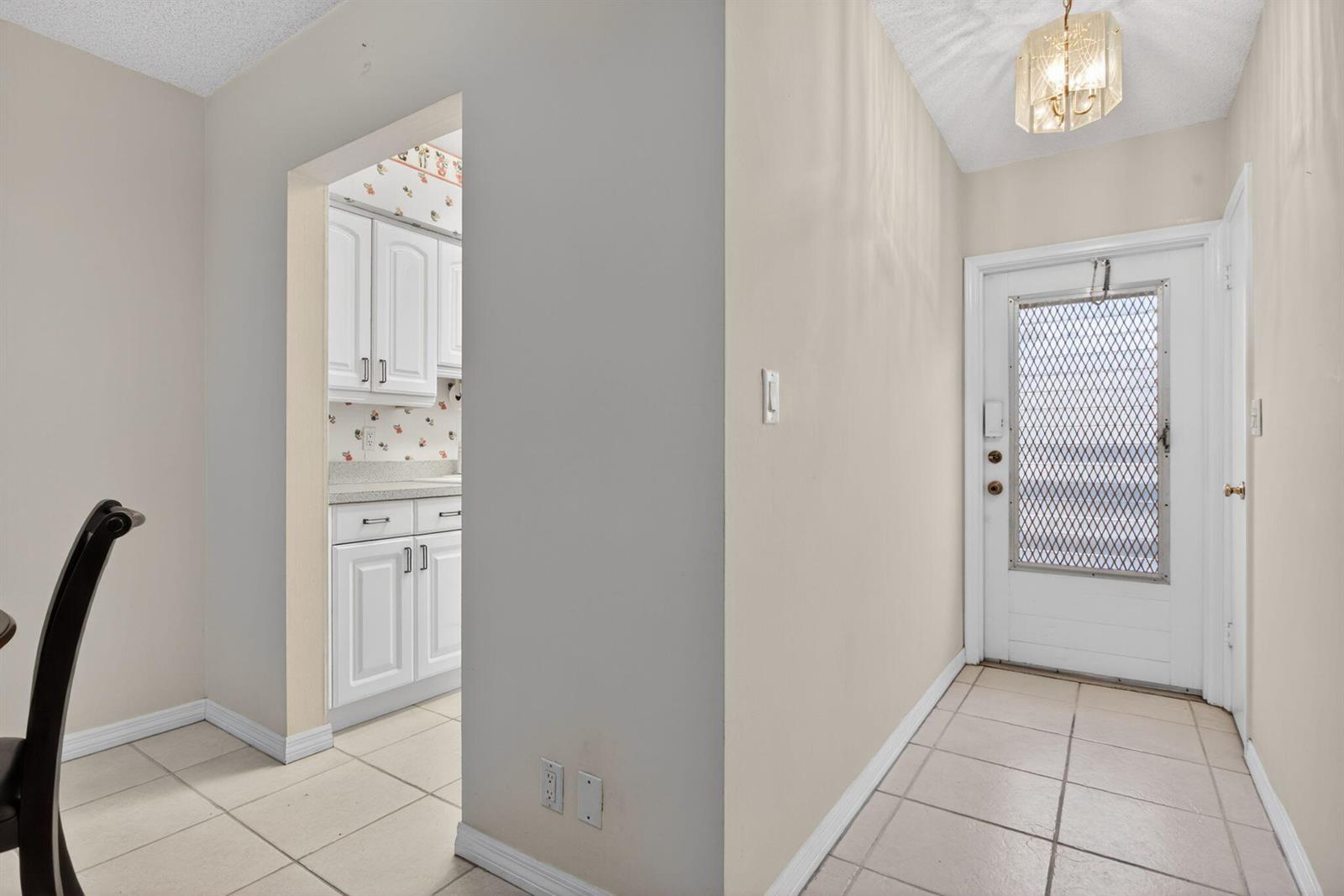 An entryway with tiled floors leads to a kitchen featuring white cabinets and floral wallpaper — 2115 NE 42nd Court # 109n, Lighthouse Point FL 33064, LIGHTHOUSE POINT, FL
