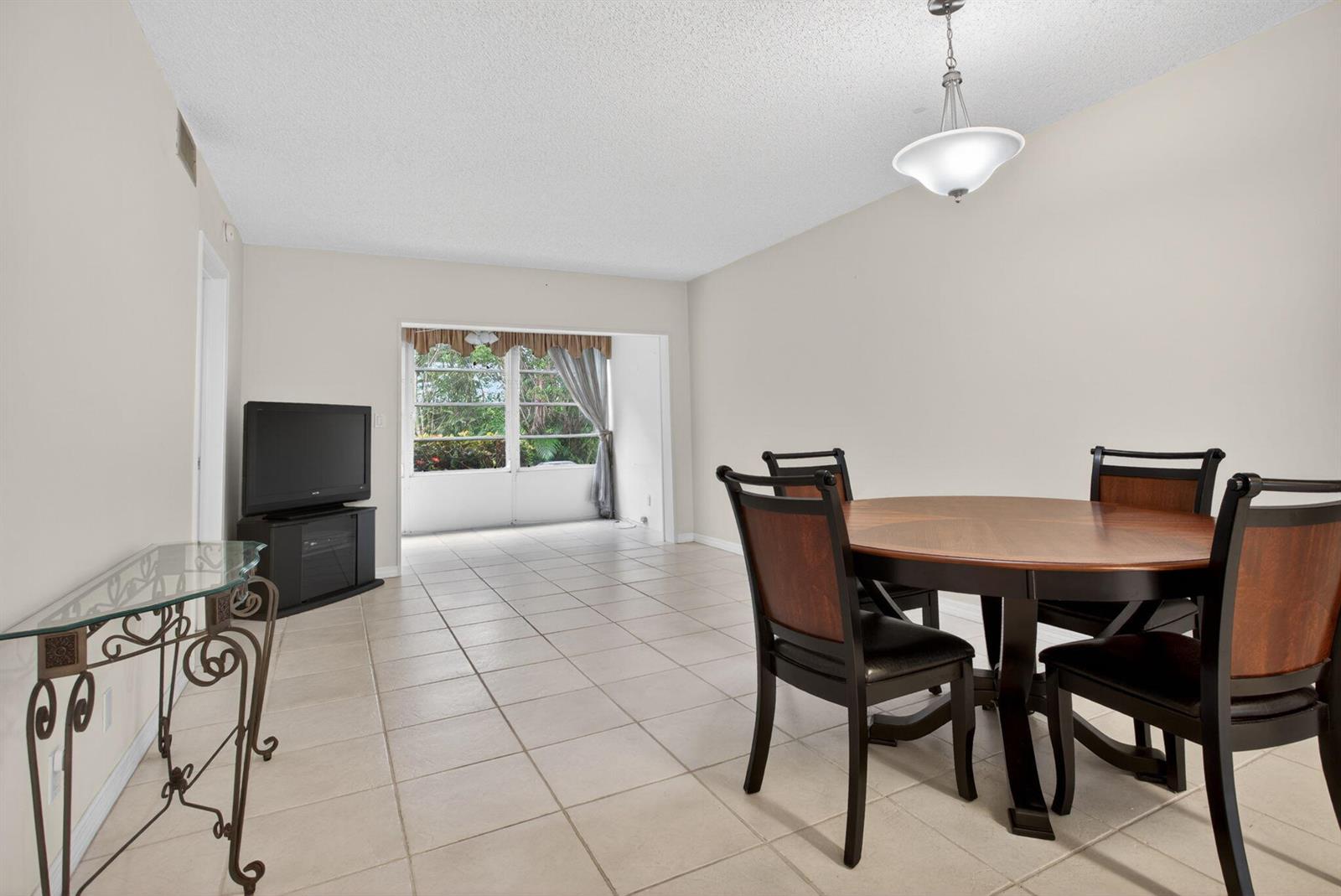A dining area with tile floors, a round wooden table, and a view of greenery — 2115 NE 42nd Court # 109n, Lighthouse Point FL 33064, LIGHTHOUSE POINT, FL