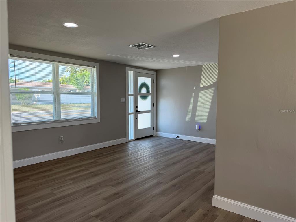 An interior view of a living room with light wood flooring, gray walls, and a door — 7220 FOX HOLLOW DRIVE, PORT RICHEY, FL